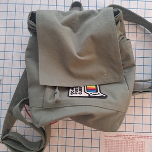 An olive green canvas backpack resting on a cutting board on the floor.