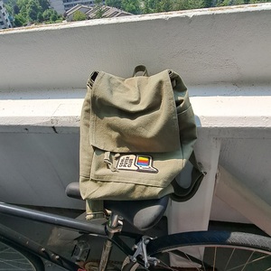 An olive green canvas backpack resting on a bike seat in an outdoor space.