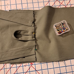 A close-up of the back of an in-progress olive bag showing straps, handles, and flap pinned in place.